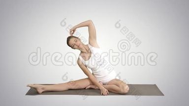 美丽的年轻女子穿着白色的衣服做瑜伽运动，坐在单腿的鸽子单鸽姿势中